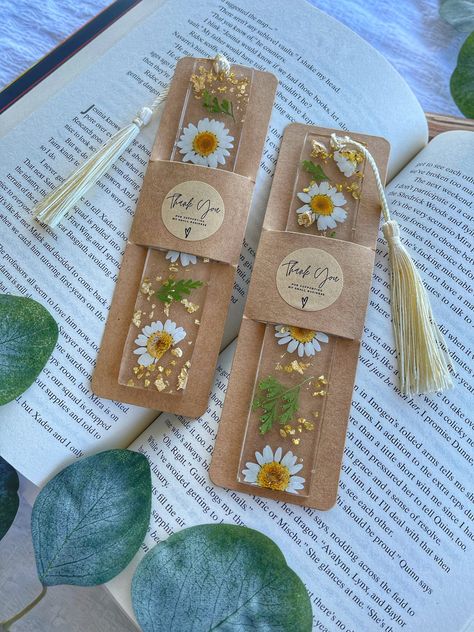 Our Dried Pressed Floral Resin Bookmarks are hand crafted pieces inspired by an endless amount of amazing novels and gardens. These bookmarks make the perfect gift for any bookworm! If you are looking for the perfect piece to elevate your reading experience -- these bookmarks are sure to enchant any reader! Details Each bookmark is hand crafted using the following: Real Pressed Flowers, Dried Pressed Leaves, Gold Flakes and Gold Stone.   Each design is unique and placements may vary as each bookmark is special in its own way. Size:  Roughly 14.6 cm x 3.3 cm Resin and Product Information:   Please note the following Information due to resin casting. Tiny air bubbles may be present within the bookmarks. These tiny air bubbles do not affect the functionality of the bookmark.  Resin made bookm Pressed Flower Resin Bookmark, Bookmark Dried Flower, Resin Flower Bookmark, Dried Leaves Crafts, Resin Bookmark Ideas, Resin Photography, Bookmark Display, Bookmark Resin, Pressed Flower Bookmark