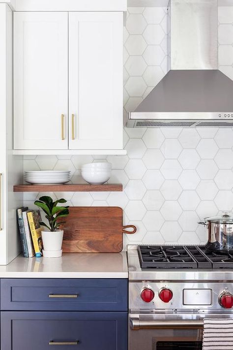 Two-toned kitchen cabinets in white upper shaker cabinets and blue lower cabinets finished with brass pulls and white hexagon backsplash tiles in a transitional cooktop design. White Upper Cabinets Dark Lower, White Hexagon Backsplash, Hexagon Tile Backsplash Kitchen, Hexagon Tile Kitchen, Dark Lower Cabinets, Two Toned Kitchen Cabinets, White Upper Cabinets, Gray Island, Hexagon Backsplash