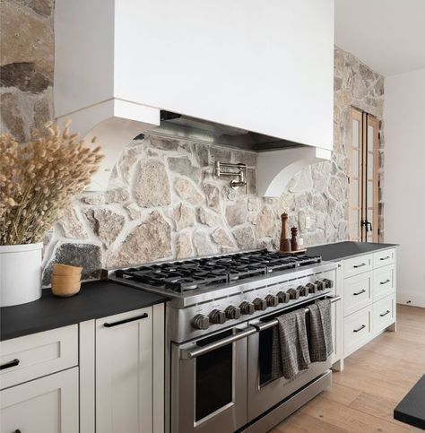 Black Countertop Stone Backsplash, Black Countertops Stone Backsplash, Stone Behind Range, Stone Accent Walls Kitchen, Gorgeous Backsplash Kitchen, White Kitchen Cabinets Black Countertops Stone Backsplash, Stone Range Hood Kitchen, Stone Backsplash Black Countertop, Stove Alcove Kitchen Stone