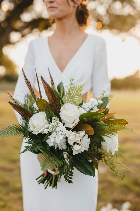 Our stunning bride, Julia, with her bridal bouquet that exudes elegant southern charm thanks to magnolia foliage, pheasant feathers and ivory roses. Two Pair Photography https://twopairphotography.com/ #bridalbouquet #magnolia #pheasant #brides #realwedding #weddingday #wedding #bastroptx Blue Fall Bouquet Wedding, Magnolia Wedding Bouquet Fall, Magnolia Wedding Decor, Pheasant Feather Bouquet, Magnolia Bouquet Wedding, Magnolia Wedding Theme, Pheasant Feather Wedding, Magnolia Bridal Bouquet, Wedding Bouquet With Feathers