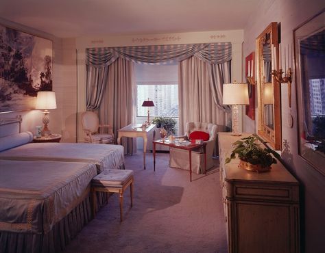 An interior view of an ornate bedroom with two double beds, gilt accented furniture, and a large window with a city view, circa 1980. 80s House Interior, 1980s Living Room, 1980s Bedroom, 80s Living Room, 1980s Interior Design, Bedroom 80s, 1980s Home Decor, 1980s Interior, 1980s Decor