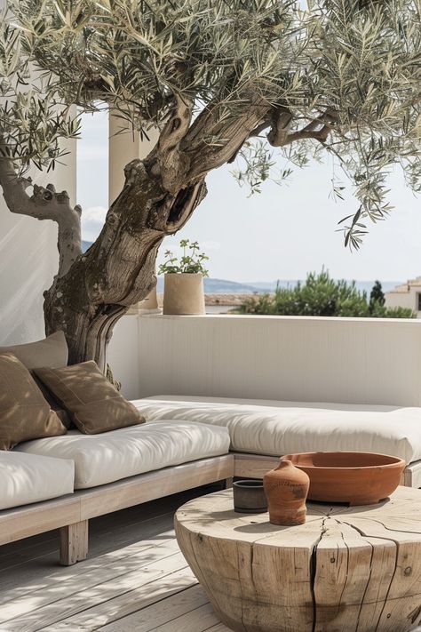 Terrasse extérieure, style méditerranéen, olive centenaire, sofa blanc, coussins couleur taupe, vue sur mer, table basse en bois brut, poterie terre cuite, atmosphère relaxante, design minimaliste, palette de couleurs naturelles, bois clair, coussins confortables, murs blancs, espace ouvert, lumière naturelle, ambiance sereine, éléments organiques, détails rustiques, sol en bois, plante grasse, ciel dégagé, ligne d'horizon, style épuré, textiles luxueux, architecture moderne, intégration naturelle, décoration éco-responsable, finitions de qualité, coin détente. Terrasse Design, Terrace Furniture, Dappled Light, Mediterranean Garden, Outdoor Inspirations, Garden Pool, Interior Garden, Menorca, Terrace Garden