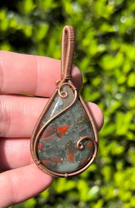 Bloodstone Copper Wire Wrapped Pendant Necklace ~ Handmade Wire Wrapped Crystals ~ Jewelry ~ Genuine stone crystal. Listing is for exact item pictured. Choose either pendant alone or included matching chain. Size Approx: 6x3cm Gemstone Type: Semi-Precious Gemstone Gift wrap optional! *Free shipping over $35 in the US* In the ancient world, Bloodstone (Heliotrope) was considered to be the most beautiful of the Jaspers, a deep, earthy green gem emboldened with spots of bright red. Called the Sun S Wire Wrapped Cabachon Pendants, How To Wire Wrap Gemstones, Rock Wire Wrapping Tutorial, Wire Wrap Stones Without Holes, Small Wire Wrapped Pendant, Copper Wrapped Crystals, Mens Wire Wrapped Jewelry, Diy Wire Jewelry Tutorials, Easy Wire Wrapping Stones