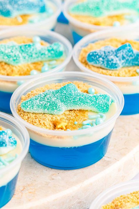 The best shark jello cups recipe - perfect for shark week or World Oceans Day with a gummy shark on top! Under The Sea Jello Cups, Ocean Jello Cups, Blue Jello With Fish, Obx Themed Snacks, Shark Themed Charcuterie Board, Shark Deserts, Shark Week Treats, Shark Jello Cups, Ocean Jello