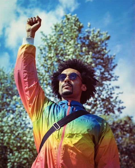 Photography by Studio PI artist, Brunel Johnson of a black man with sunglasses on and his afro hair let loose. Fist in the air, wearing a rainbow coloured raincoat with a crossbody bag. Street Portraits, Street Portrait, Documentary Photographers, Afro Hairstyles, Lionel Messi, Skin Color, London Uk, Street Photography, Documentaries