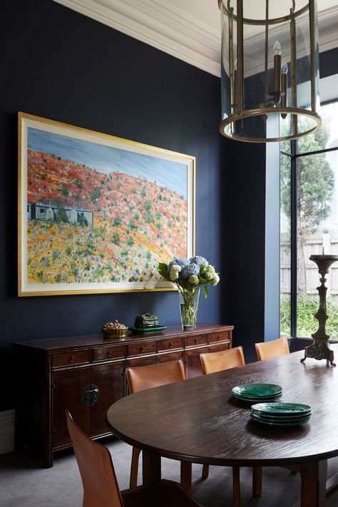 This traditional home was given a colourful makeover! Done by the team at Brownlow Interior Design, this beautifully restored period home was updated using a bold colour palette. This dark blue dining room features a dark wood dining table, leather chairs, green plates, grogeous abstract landscape artwork and a stunning dark brown wood cabinet on the side. To find the full home tour, click on the pin or go to StyleCurator.com.au. Victorian Italianate House, Dark Blue Dining Room, Dark Wood Dining Room, Decorating With Antiques, Italianate House, Dark Wood Dining Table, Antique Bedside Tables, Maple Dining Table, Dark Dining Room