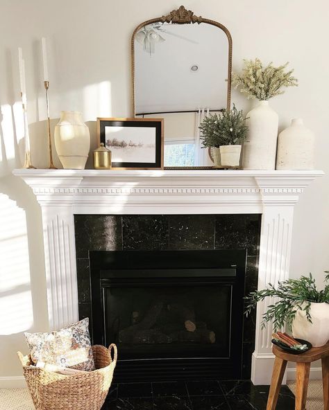 Neutral decor, such as the brass mirror and wooden photo frame, add a slight color accent to this monochrome white and black living room. The white stone vases on the mantel create an elegant, seamless look that blends perfectly with the white walls and mantel. Elevate the decor with gold-plated candle holders for a timeless aesthetic. Mantel Tv Decor, Mantel Decorating Ideas Picture Frames, White Fireplace Mantels Decor, White Tv Mantle, Styling Mantle With Mirror, Mantel Decorating Ideas With Pictures, Fireplace Decor Mirror, White Fireplace Mantle Decor, White Mantle Decorating Ideas