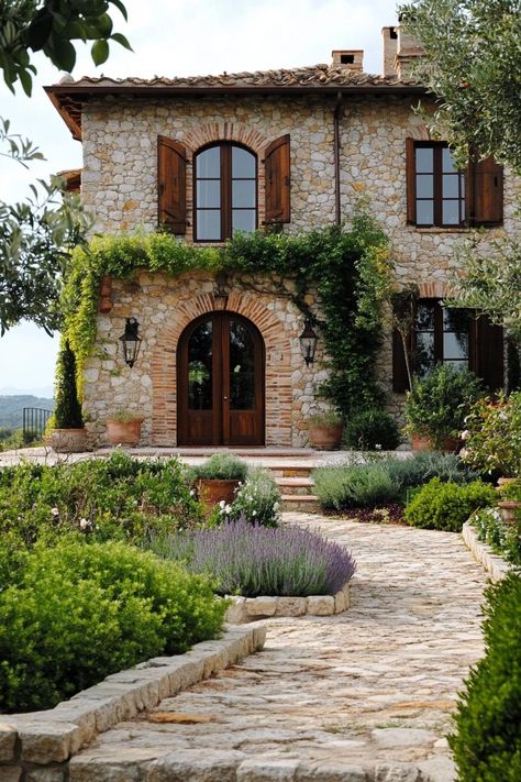 Modern Tuscan mediterranean house stone facade with wooden arched doorway lush Tuscany garden. Check out all of these stunning Tuscan Mediterranean houses that look like sun-drenched villas straight out of Italy. Italy Stone House, Small Tuscan House Plans, Rustic Italian Aesthetic, Italian Exterior Design, Tuscany Italy Homes, Modern Italian Farmhouse Exterior, Italian Lake House, Tuscan Mediterranean Homes, Tuscan Villa Floorplan