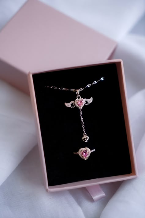 Discover the elegance and romance of our Heart's Desire Jewelry Set! This stunning set includes a delicate necklace and a matching ring, both showcasing exquisite heart-shaped pink gemstones surrounded by brilliant clear stones. The necklace features a lovely winged design on either side of the pendant, symbolizing freedom and beauty, and a little dangling heart for added charm. The ring echoes this design, with a striking heart-shaped pink gemstone embraced by sparkling clear stones. ✨ **Unique Tangled Jewelry, Simplistic Jewelry, Ring Gift Box, Unique Valentines Day Gifts, Pretty Jewelry Necklaces, Magical Jewelry, Jewelry Accessories Ideas, Heart Gemstone, Set Necklace