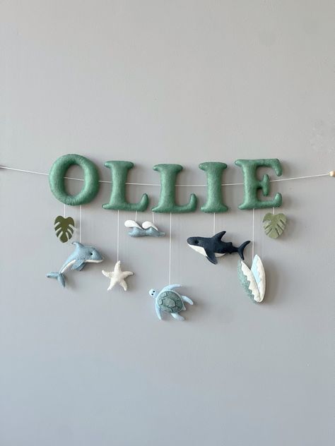 "Are you looking for a special and unique present for your loved ones? How about a baby name garland? A personalized safari name banner is the sweetest addition to any space in your home or given as a new baby gift. This personalized baby name sign will add the perfect finishing touch to your baby boy nursery, at a safari birthday party, or as a decorative accessory for photo props. INCLUDES Please select the number of letters in the name from the dropdown menu. Banner includes: ● letters, ● One main item per one letter. Please specify the main items (bear, fox, hare, deer, owl, tree) in the personalization window. ● additional items: leaves, triangles, little foil stars, clouds We will send you a photo before shipping =) This item made by hand - no machines involved. We hand-cut, hand-sew Seal Themed Nursery, Name Plate Nursery, Ocean Themed Baby Room, Otter Themed Nursery, Beach Boy Nursery, Baby Boy Ocean Theme Nursery, Above Crib Decor Boy, Nursery Sea Theme, Baby Room Name Signs