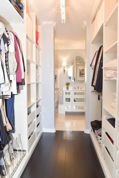 Gorgeous galley-style custom walk-in closet is fitted with a dark stained wood floor flanked by modular styled shelves fitted above white drawers and beside clothing rails. Doorless Walk In Closet, Galley Walk In Wardrobe, Narrow Long Closet, Closet To Bathroom Walk Through, Small Walk Through Closet To Bathroom, Galley Walk In Closet, Walkthrough Closet To Bathroom, Walk Through Closet To Bathroom Layout, Bathroom And Closet Combo Master