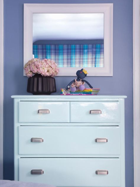 An icy blue four-drawer dresser is used to display a small purple floral bouquet inside a brown pot, a stuffed monkey and a handful of Dr. Seuss books, while above hangs a large white mirror in which you can see the reflection of a blue and purple plaid valance. The color schemes compliment the purple hue of the room walls. Periwinkle Bedroom, Large White Mirror, Lowes Paint Colors, Lowes Paint, Refurbished Dresser, Lacquered Furniture, Designers Portfolio, Eclectic Kids Room, Interior Remodeling