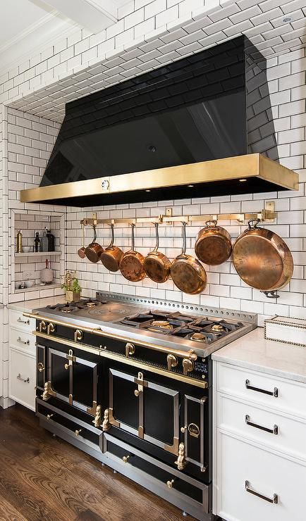 A subway tiled cooking nook is filled with a black kitchen hood with brass trim placed over a brass pot rack mounted on the backsplash as well as a black French stove, La Cornue Grand Palais 180. French Stove, Black Stove, Trendy Kitchen Tile, French Kitchen Decor, Desain Pantry, Bohemian Kitchen, Kitchen Hoods, Primitive Kitchen, French Kitchen