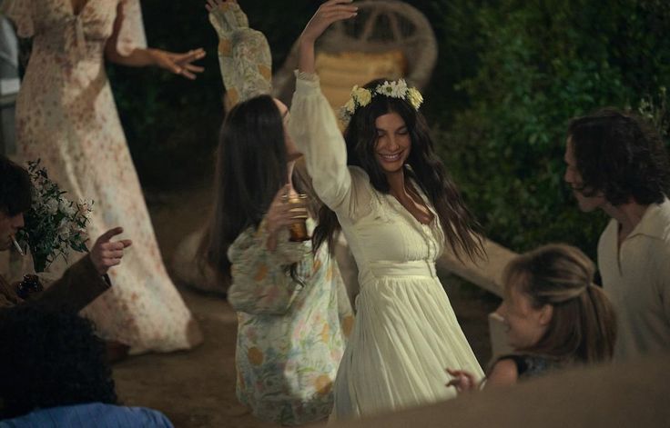 a woman in a white dress is dancing with other people around her and holding hands up