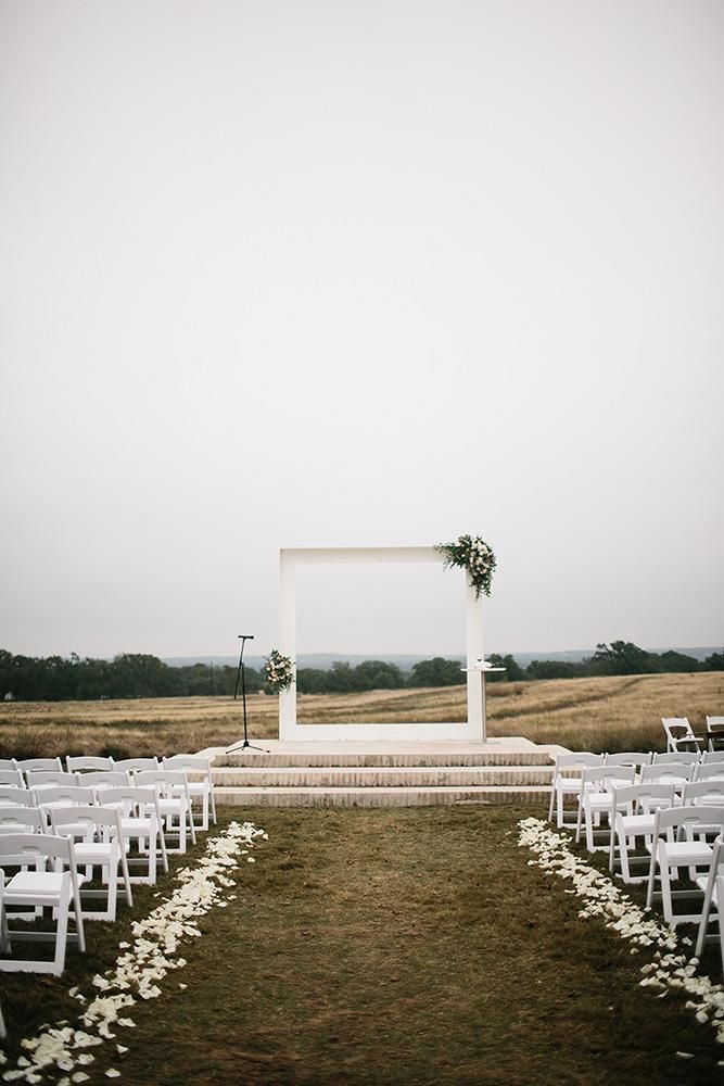 an outdoor ceremony set up with white chairs and flowers