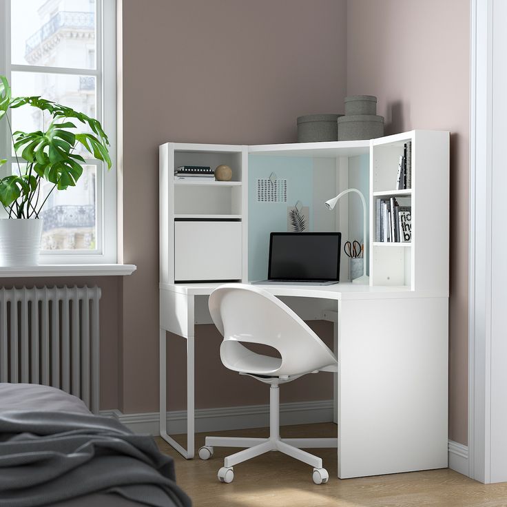 a white desk with a laptop on it in a room next to a bed and window