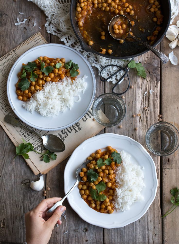 two white plates topped with rice and chickpeas next to a pot of stew