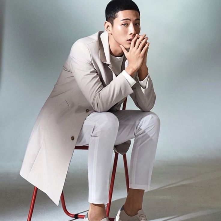 a man sitting on top of a red chair in front of a gray background with his hands clasped