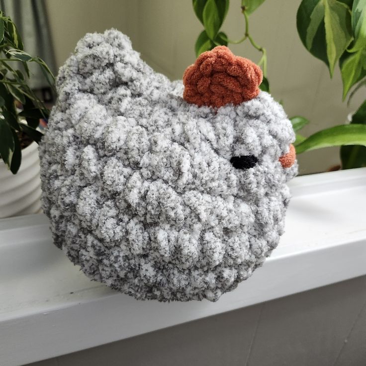 a crocheted chicken sitting on top of a window sill next to a potted plant