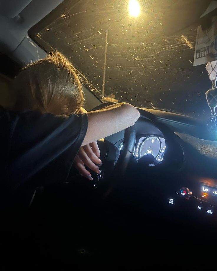 a man driving a car at night with his hand on the steering wheel and light shining from behind him