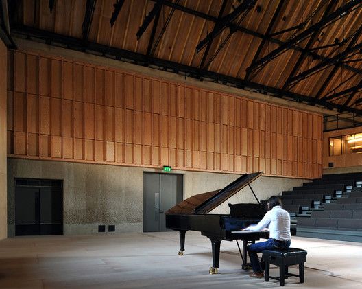 a man sitting at a piano in an empty room with wooden paneled walls and stairs