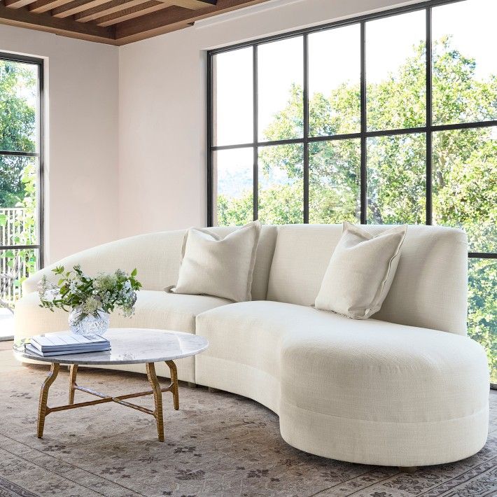 a living room with large windows and a white couch in front of a table on top of a rug