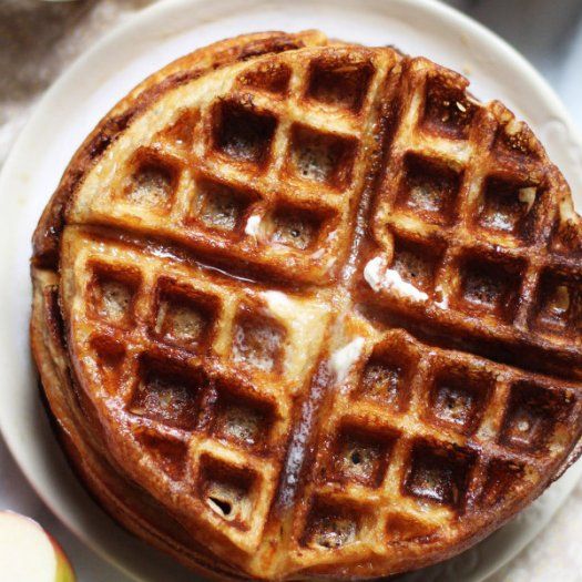 a waffle on a plate next to an apple