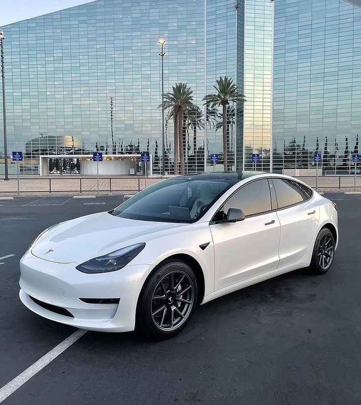 a white electric car parked in a parking lot next to a tall building and palm trees