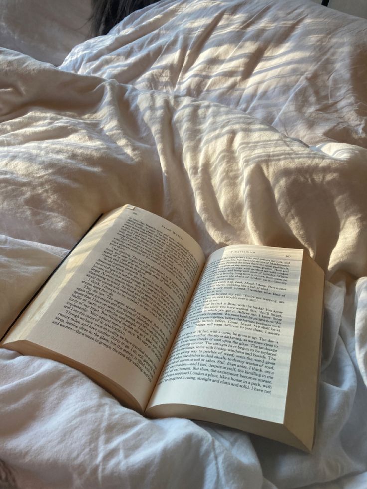 an open book laying on top of a bed next to a white comforter and pillows