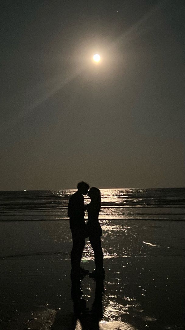 two people are kissing on the beach at night