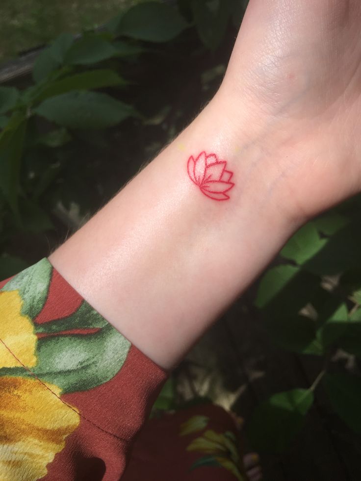 a woman's wrist with a small red flower tattoo on the left side of her arm