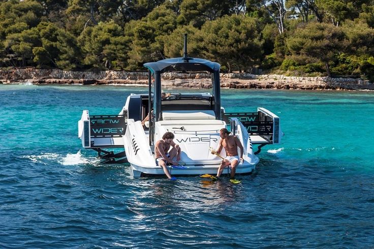 two people are sitting on the back of a boat in the blue water near some trees