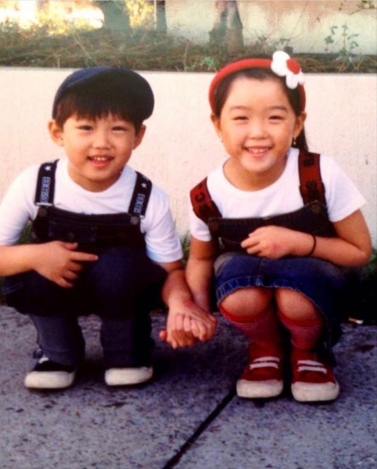 two young children sitting next to each other on the ground with their hands in their pockets