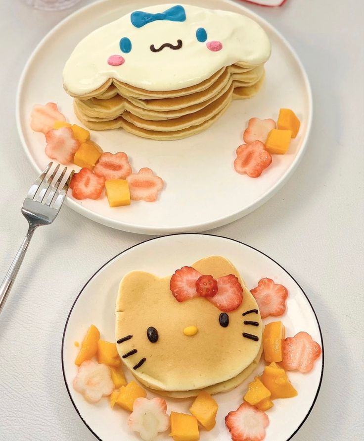 two plates with pancakes decorated like hello kitty and one has fruit on the plate as decoration