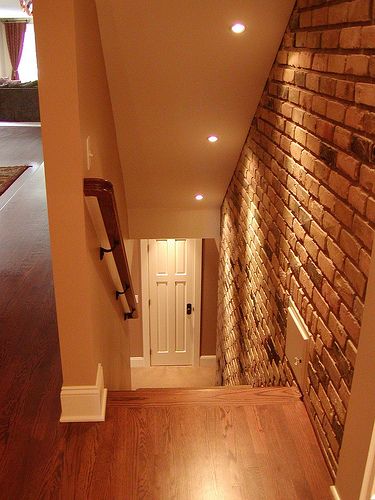 an empty room with wood flooring and brick wall in the corner, next to a white door