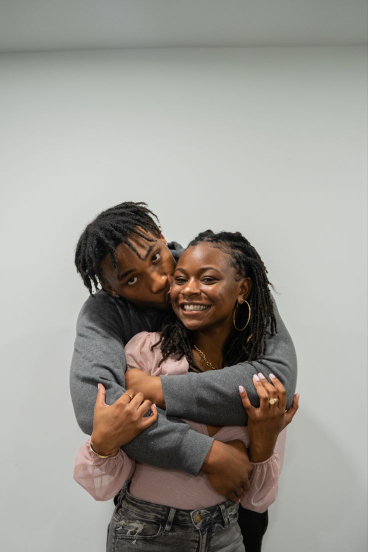 two women hugging each other in front of a white wall and one woman has her arms around the other