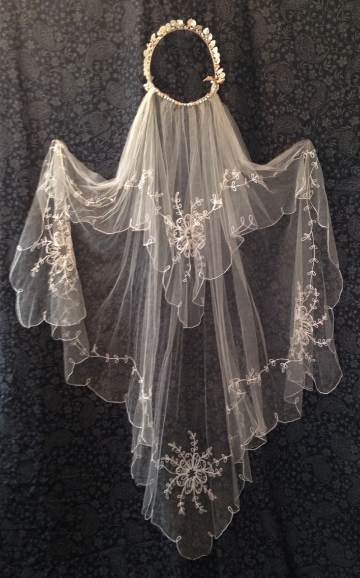 a white veil with flowers on it hanging from a wall next to a black background