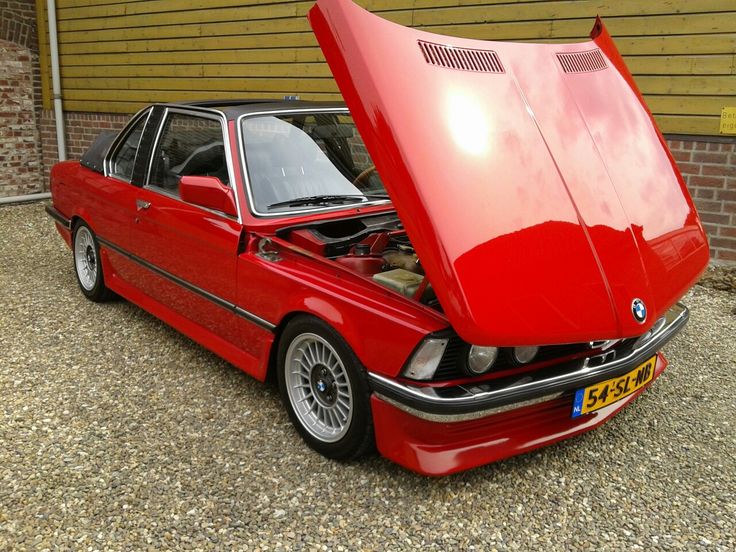 a red car with its hood open in front of a garage