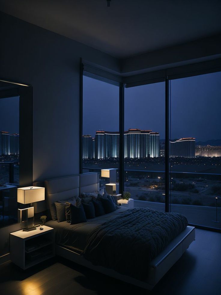 a bed sitting in a bedroom next to two large windows with city lights on them