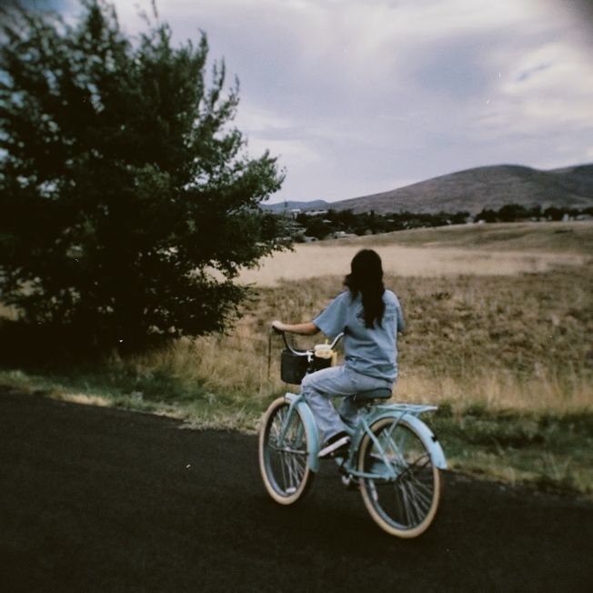 girl riding blue bike with basket on the street with mountain scenery Aesthetic Bikes With Basket, Riding A Bicycle Aesthetic, Bike Pictures Aesthetic, Blue Bike With Basket, Bike With A Basket, Bike Riding Astethic, E Bike Aesthetic, Bike With Basket Aesthetic, Bicycle Ride Aesthetic