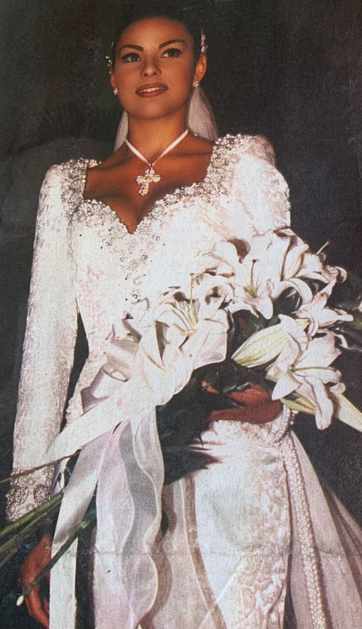 a woman in a white wedding gown holding a bouquet of flowers and wearing a tiara