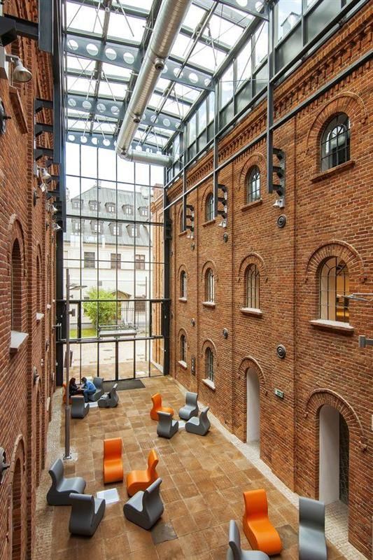 the interior of an industrial building with orange and gray chairs on the floor, windows, and brick walls