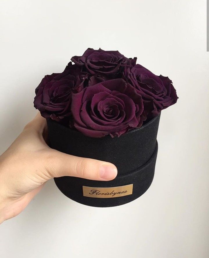 a hand holding a black hat with purple roses