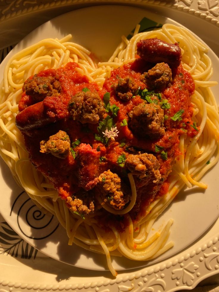 a heart shaped pasta dish with meatballs and tomato sauce on a white plate in the shape of a heart