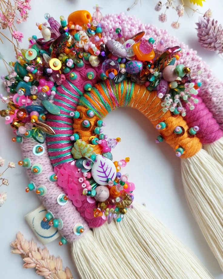 an assortment of colorful beads and tassels on a white surface next to flowers