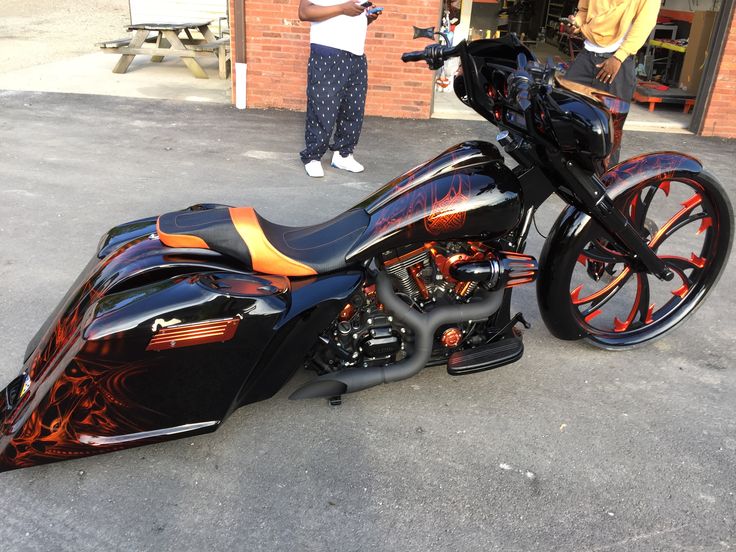 a black and orange motorcycle parked in front of a brick building with people standing around