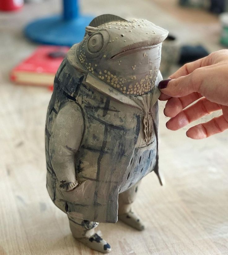 a hand holding a small ceramic animal on top of a wooden table