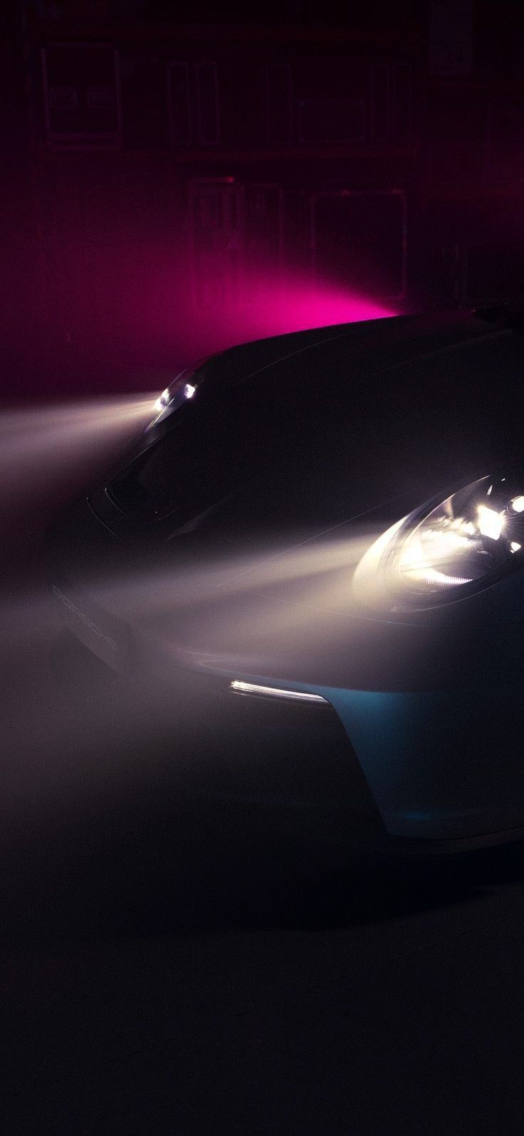 a sports car driving on a foggy road in the dark with its headlights up