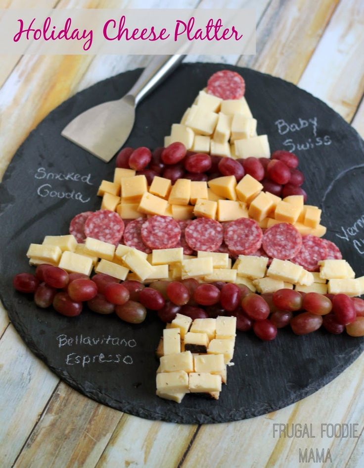 a holiday cheese platter with sausages, grapes and crackers on a slate board