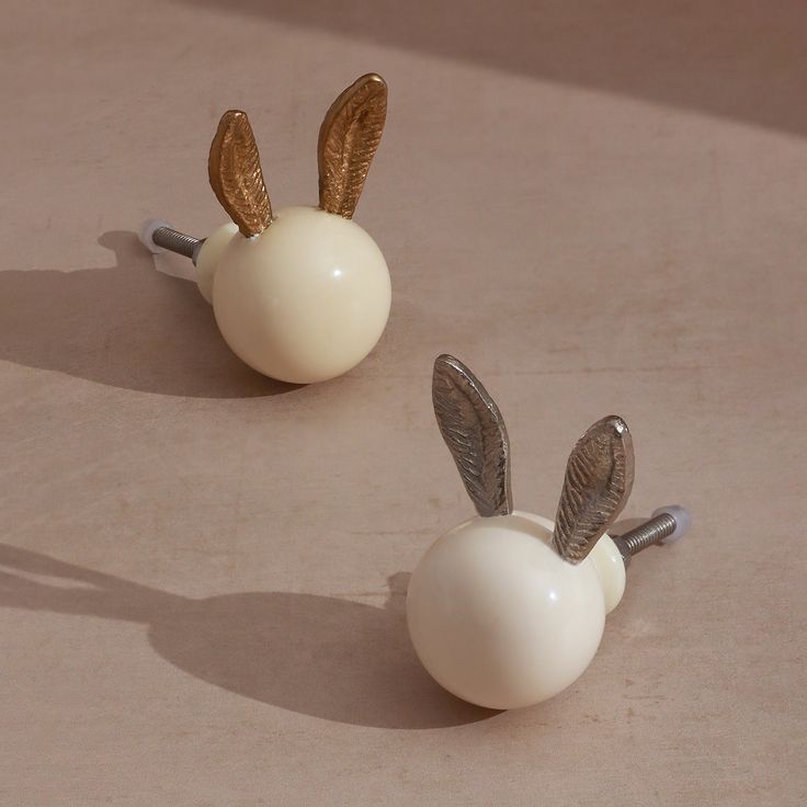 two white ceramic objects with gold colored metal ears on each one, sitting on a beige surface